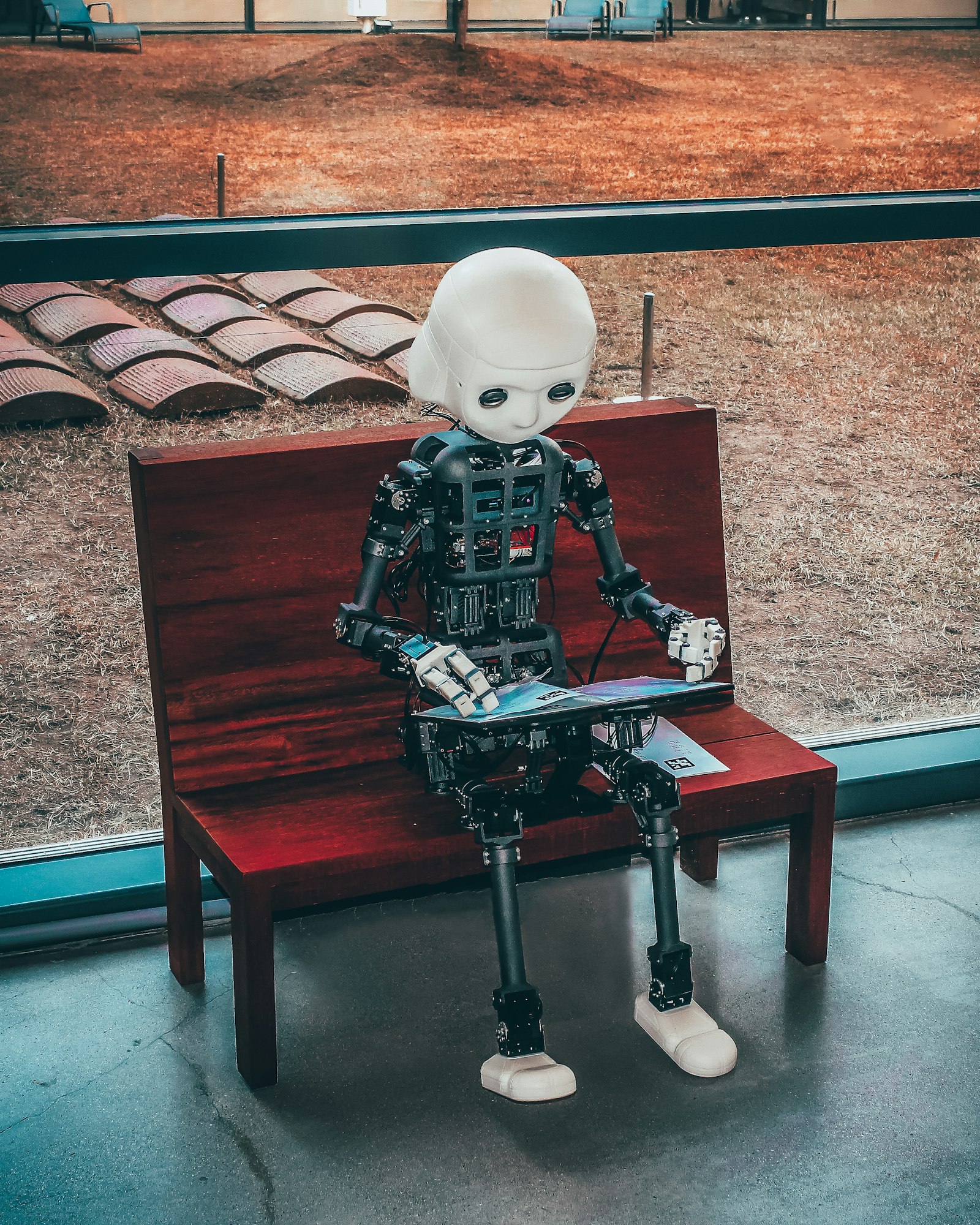 A humanoid robot sitting on a bench reading a magazine